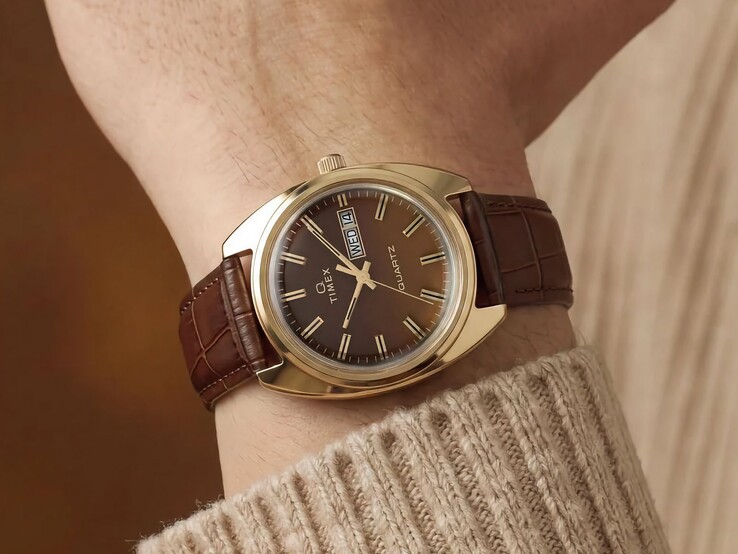 Kahverengi fumé kadranı ve altın tonlu kasasıyla Timex Q 1976 Day and Date, kahverengi deri kayışla bir bilekte gösteriliyor.