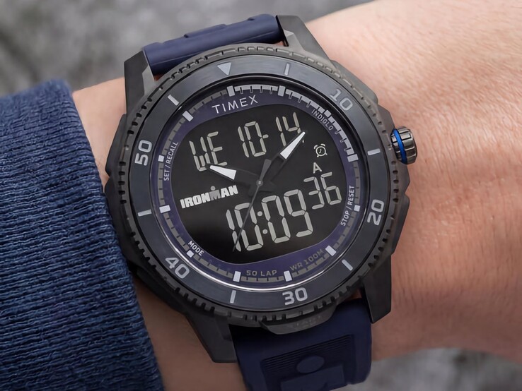 Koyu mavi kayışlı ve mavi kurma kolu detayı bulunan siyah Timex Ironman Adrenaline analog-dijital saat, bir bilekte gösterilmiştir.