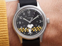Timex MK1'in siyah kadranının yakın çekimi; sarı-siyah kareli bir arka plan üzerinde Snoopy figürü, Arap rakamlı saat işaretleri ve ışıklı ibreler görülüyor.