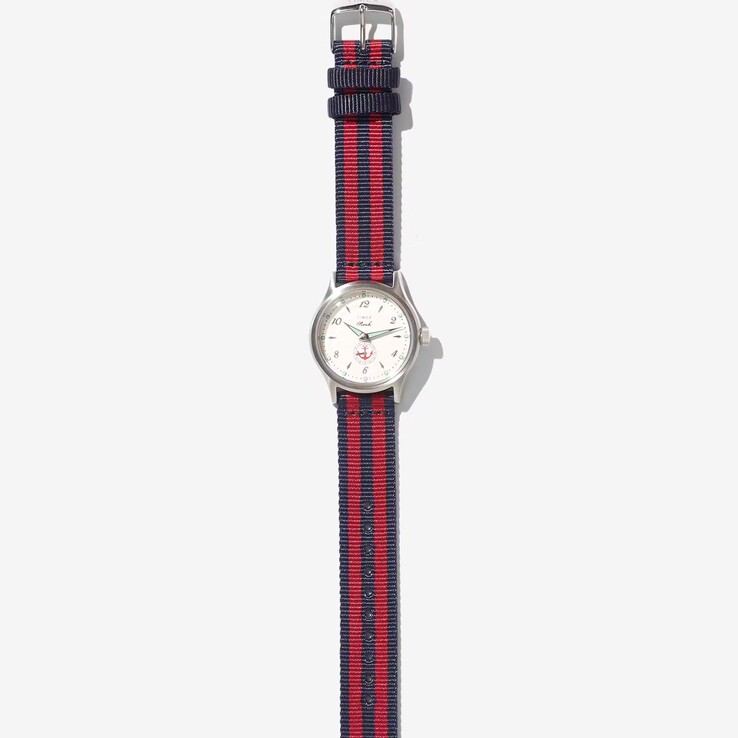 Noah x Timex MK1 Anchor saat: gümüş rengi 36 mm kasa, krem rengi kadran, çapa grafiği ve lacivert-kırmızı çizgili kumaş kayış.