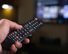 Arka planda bulanık bir TV varken uzaktan kumanda tutan el