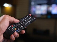 Arka planda bulanık bir TV varken uzaktan kumanda tutan el