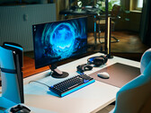 Beyaz bir masanın üzerinde Sony Inzone M10S II monitörün yer aldığı, dikey konumda duran bir PlayStation 5 Pro konsolu, mekanik klavye, kablosuz fare ve hafif mavi ışıklı bir kulaklık içeren sade bir stüdyo oyun kurulumudur.