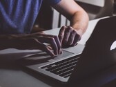 Loş ışıkta bir MacBook klavyesinde yazan eller, parlayan Apple logosu