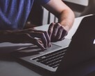 Loş ışıkta bir MacBook klavyesinde yazan eller, parlayan Apple logosu
