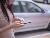 Arka planda gümüş renkli bir araba varken akıllı telefonunda yazı yazan bir kadın