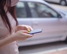 Arka planda gümüş renkli bir araba varken akıllı telefonunda yazı yazan bir kadın