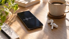 Ahşap bir masa üzerinde kablosuz kulaklıklar ve bir kahve fincanının yanında ses dalga biçimini gösteren bir akıllı telefon