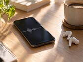 Ahşap bir masa üzerinde kablosuz kulaklıklar ve bir kahve fincanının yanında ses dalga biçimini gösteren bir akıllı telefon