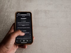 Gri taş bir yüzeyin üzerinde ChatGPT arayüzünü gösteren bir akıllı telefonu tutan el