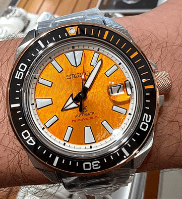 Seiko Prospex HBB005K1 modelinin yakın çekim görüntüsü; dokulu kehribar renkli kadranı, büyük boyutlu ışıklı saat işaretleri, geniş ibreleri, tarih penceresi ve turuncu işaretli siyah dalış çerçevesini göstermektedir.