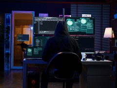 Kapüşonlu bir araştırmacı karanlık bir ortamda birden fazla ekran üzerinde çalışıyor. Jenerik hacker resimde. 
