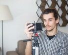 Genç bir adam, tripoda monte edilmiş bir akıllı telefonla evde kendi videosunu çekiyor