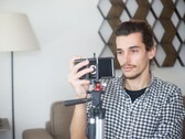 Genç bir adam, tripoda monte edilmiş bir akıllı telefonla evde kendi videosunu çekiyor