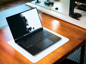 Sıcak tonlu ahşap bir masanın üzerinde, beyaz bir masa örtüsünün üzerine yerleştirilmiş, açık mat siyah renkli bir Razer Blade 16 oyun dizüstü bilgisayarı, canlı siyah-beyaz bir duvar kağıdı görüntülüyor.