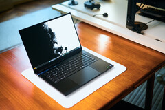 Sıcak tonlu ahşap bir masanın üzerinde, beyaz bir masa örtüsünün üzerine yerleştirilmiş, açık mat siyah renkli bir Razer Blade 16 oyun dizüstü bilgisayarı, canlı siyah-beyaz bir duvar kağıdı görüntülüyor.