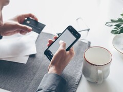 Bir elinde banka kartını tutarken diğer eliyle akıllı telefona dokunan kişi