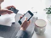 Bir elinde banka kartını tutarken diğer eliyle akıllı telefona dokunan kişi