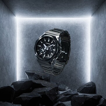 G-Shock GST-B1000BD-1A, beton bir teşhir alanında koyu renkli kayaların üzerinde asılı duruyor ve siyah paslanmaz çelik yapısını öne çıkarıyor.