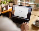 Google ana sayfası açık bir dizüstü bilgisayarın başında oturan, yanında bir fincan kahve bulunan kişi