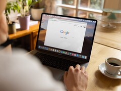 Google ana sayfası açık bir dizüstü bilgisayarın başında oturan, yanında bir fincan kahve bulunan kişi