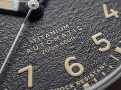 Timex Expedition Field Post Titanium saatinin, Arap rakamları, ışıklı ibreler ve saat işaretleri ile tarih penceresi bulunan dokulu siyah kadranının yakın çekimi.