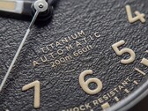 Timex Expedition Field Post Titanium saatinin, Arap rakamları, ışıklı ibreler ve saat işaretleri ile tarih penceresi bulunan dokulu siyah kadranının yakın çekimi.