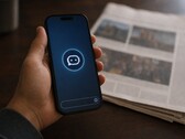 Bir el, üzerinde sohbet robotu simgesi bulunan bir akıllı telefonu tutuyor; yanında basılı bir gazete duruyor.