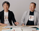 Shigru Miyamoto ve Tezuka Takashi'nin Super Mario Bros. 30. yıl dönümü tişörtleri giyerken çekilmiş bir ekran görüntüsü