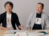Shigru Miyamoto ve Tezuka Takashi'nin Super Mario Bros. 30. yıl dönümü tişörtleri giyerken çekilmiş bir ekran görüntüsü