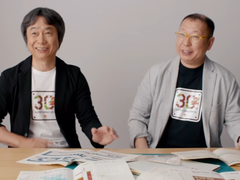 Shigru Miyamoto ve Tezuka Takashi'nin Super Mario Bros. 30. yıl dönümü tişörtleri giyerken çekilmiş bir ekran görüntüsü