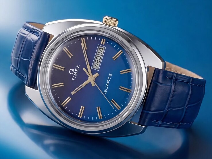 Timex Q 1976 Day and Date'in mavi degrade kadranını, cilalı paslanmaz çelik kasasını ve altın tonlu kurma kolunu öne çıkaran açılı ürün çekimi.