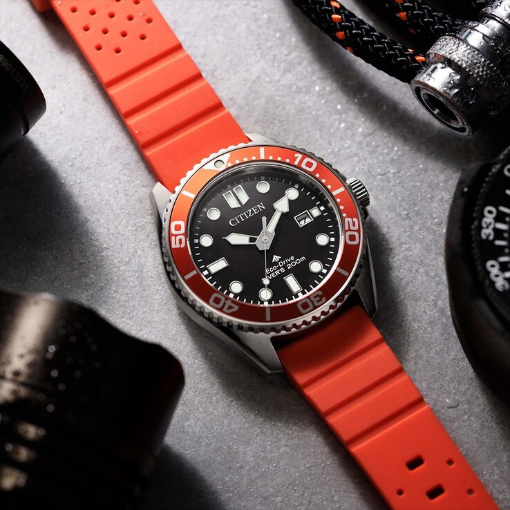 Siyah kadranlı, turuncu çerçeveli ve turuncu kayışlı Citizen Promaster Marine BN0268-01E dalış saati, dokulu bir yüzey üzerinde fotoğraflanmıştır.