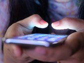 Loş ışıkta, ekranı parlayan bir akıllı telefonu tutan iki el