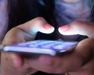 Loş ışıkta, ekranı parlayan bir akıllı telefonu tutan iki el