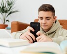 Önünde açık okul kitapları bulunan, kapüşonlu bir genç, akıllı telefonunda yazıyor.