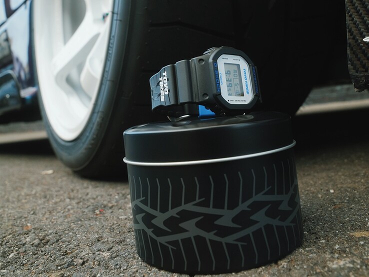 Casio G-Shock DW5600TT25-1 x Toyo Tires saat, bir araba jantının yanında, lastik temalı metal bir kutunun üzerinde sergileniyor.