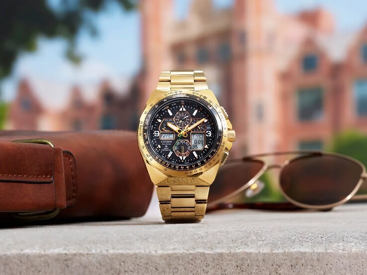 Citizen Promaster Skyhawk A-T JY8144-50E altın rengi pilot saati, arka planda bulanık bir şehir manzarası eşliğinde, kahverengi deri çanta ve güneş gözlüğünün yanındaki bir çıkıntıya dik olarak yerleştirilmiştir.