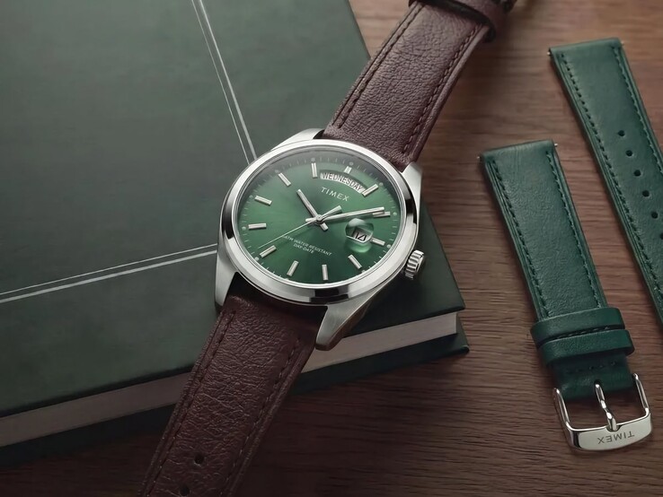 Yeşil kadranı ve kahverengi deri kayışıyla Timex Legacy Day and Date, değiştirilebilir yeşil deri kayışın yanında koyu yeşil bir kitabın üzerinde sergileniyor.