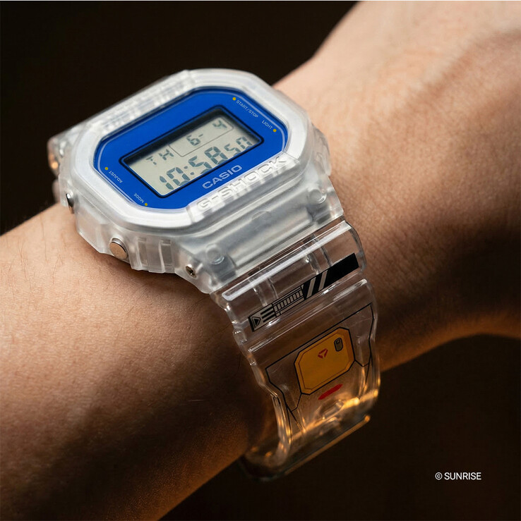 Bileğe takılan Casio G-Shock x Mobile Suit Gundam DW-5600GM26-7DR, şeffaf reçine kasa ve kayış, mavi çerçeve çevresi ve kayış üzerinde Gundam'dan ilham alan grafiklere sahiptir.