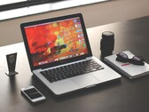 Koyu renkli bir masada, akıllı telefon, gözlük ve not defterinin yanında MacBook Pro