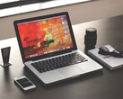 Koyu renkli bir masada, akıllı telefon, gözlük ve not defterinin yanında MacBook Pro