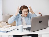 Bir dizüstü bilgisayarın önünde kulaklık takan ve hayal kırıklığıyla ellerini kaldıran adam