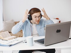 Bir dizüstü bilgisayarın önünde kulaklık takan ve hayal kırıklığıyla ellerini kaldıran adam