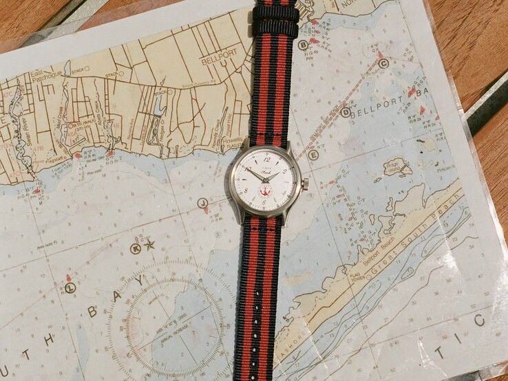 Noah x Timex MK1 Anchor saat, deniz haritası üzerinde duran lacivert ve kırmızı çizgili kumaş kayışla birlikte.