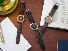 Bir defter, kalem, lamba ve açık bir kitabın yanında ahşap bir masanın üzerinde dizilmiş üç adet Citizen Rolan saat; bunların arasında somon rengi kadranlı AW2110-14Z modeli de bulunuyor.