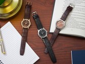 Bir defter, kalem, lamba ve açık bir kitabın yanında ahşap bir masanın üzerinde dizilmiş üç adet Citizen Rolan saat; bunların arasında somon rengi kadranlı AW2110-14Z modeli de bulunuyor.