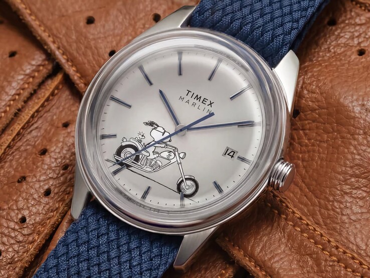 Peanuts x Timex Marlin Jet Automatic Easy Rider saatinin önden açılı görünümü; kubbe şeklindeki cam, gümüş tonlu paslanmaz çelik kasa, Snoopy temalı kadran ve mavi kumaş kayışı öne çıkmaktadır.