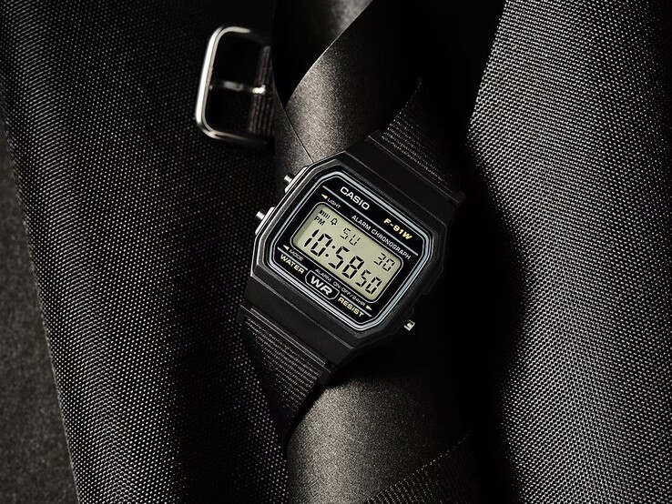 Siyah kasalı, siyah dokuma kumaş kayışlı ve gümüş renkli detaylara sahip Casio F-91WF-1A dijital saat, koyu renkli dokulu bir arka plan önünde fotoğraflanmıştır.