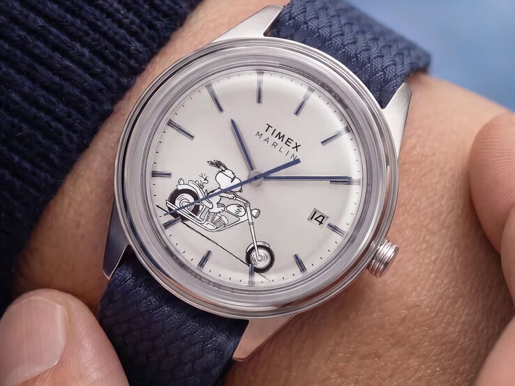 Bileğe takılmış Peanuts x Timex Marlin Jet Automatic Easy Rider saatinde, gümüş-beyaz kadran üzerinde motosiklet süren Snoopy, mavi indeksler ve ibreler ile mavi dokuma kumaş kayış görülmektedir.